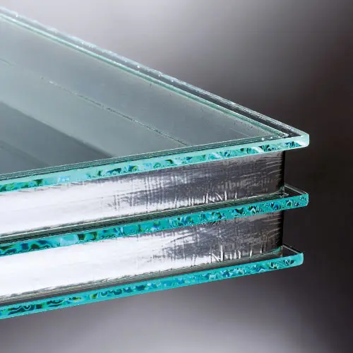 A close-up view of three stacked, double-glazed glass panels, showcasing the transparent layers with a slight green tint along the edges, against a gradient gray background.